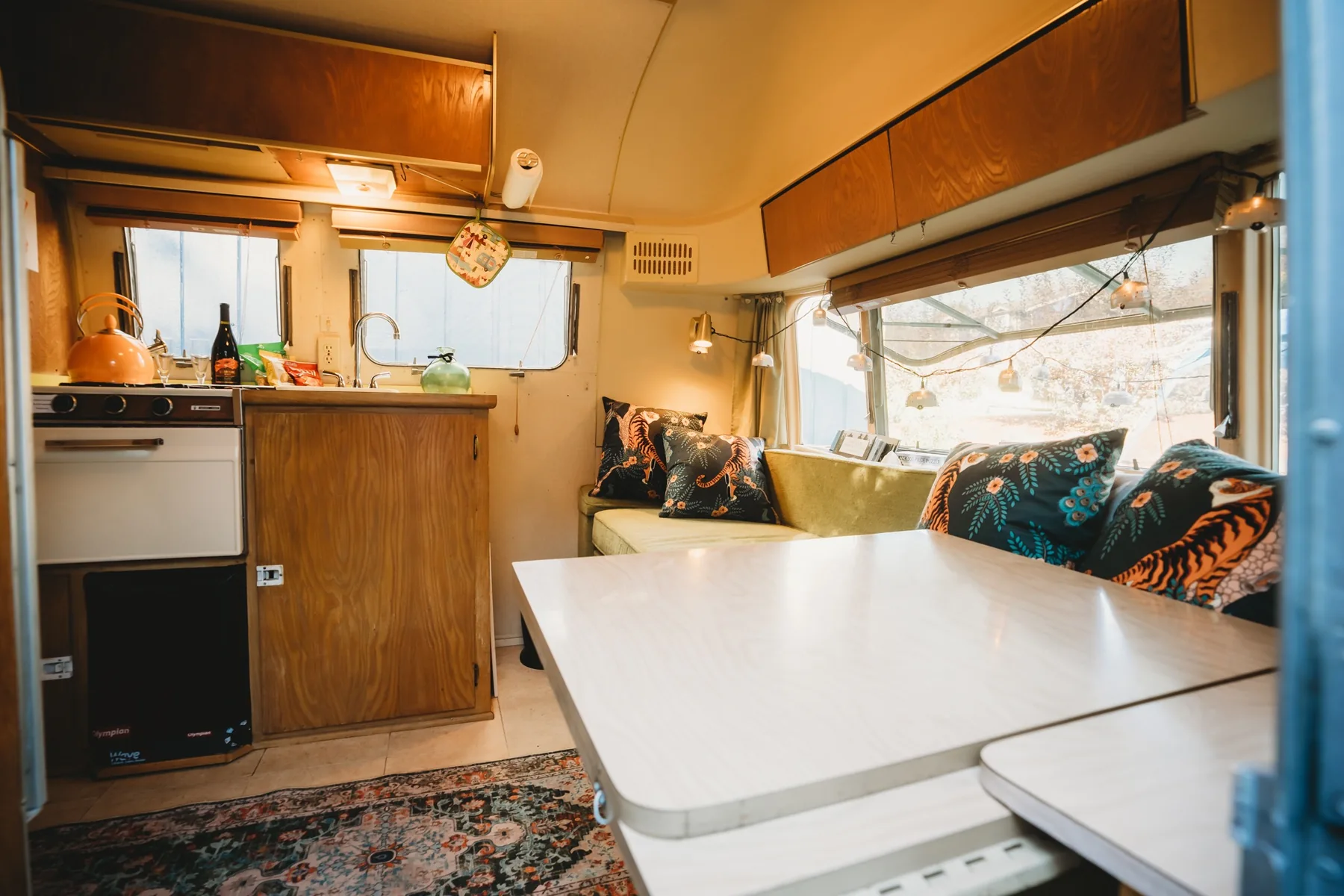 Caravel interior with green sofa, tiger-patterned cushions, pale dining table and warm wood cabinets
