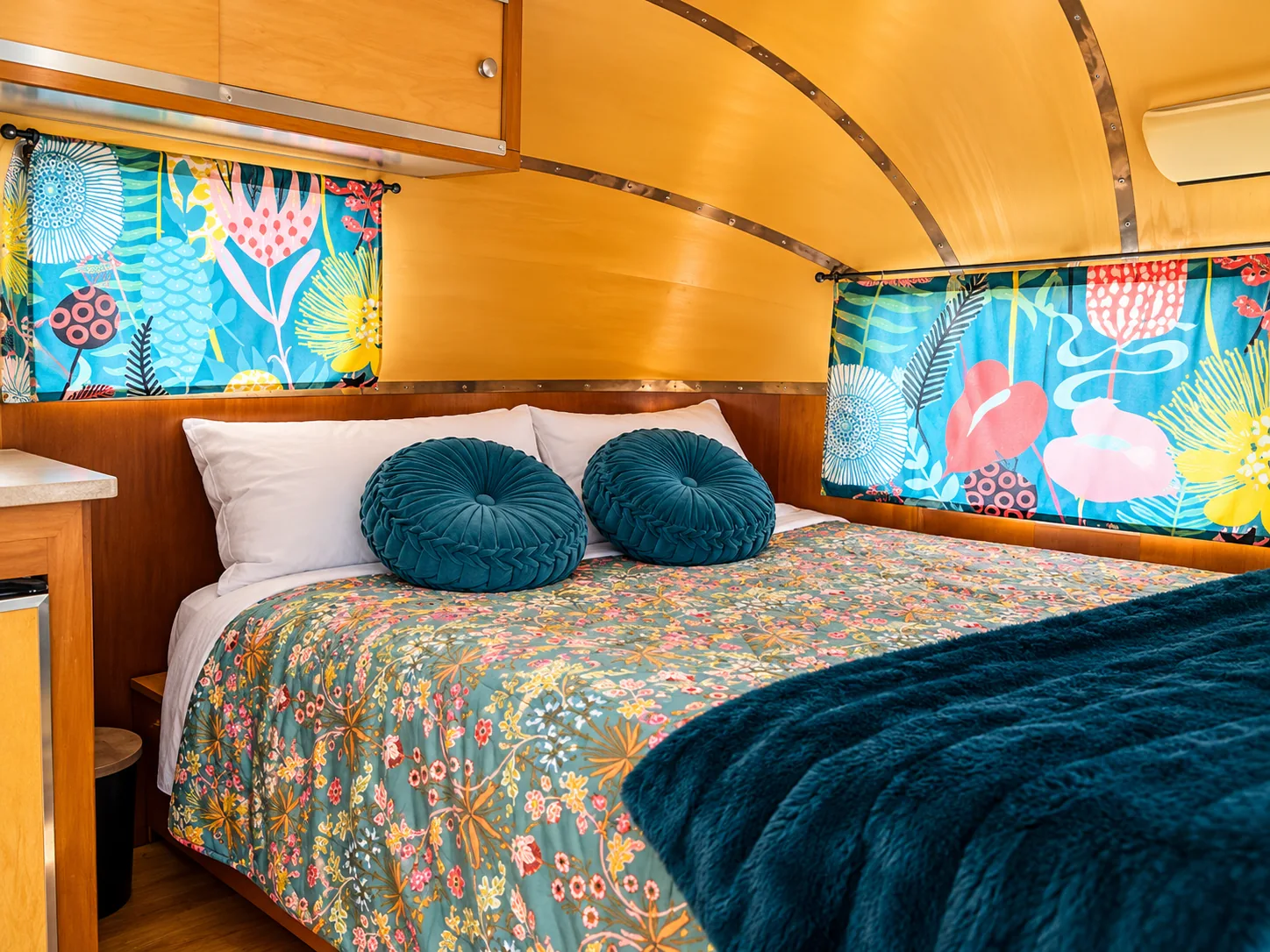 Safari bedroom with floral coverlet, teal round pillows and bright printed curtains